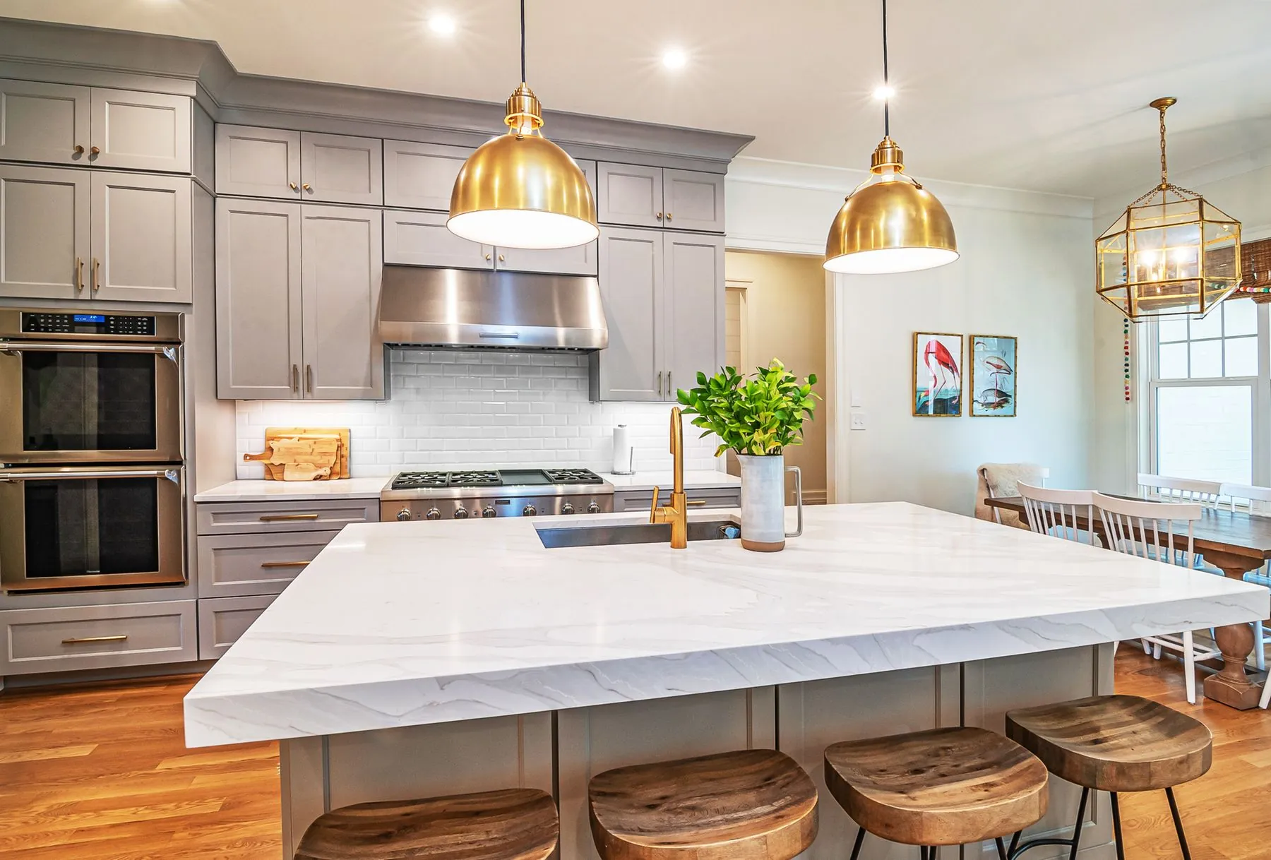 A pale kitchen with a marble island and three brass pendant lights